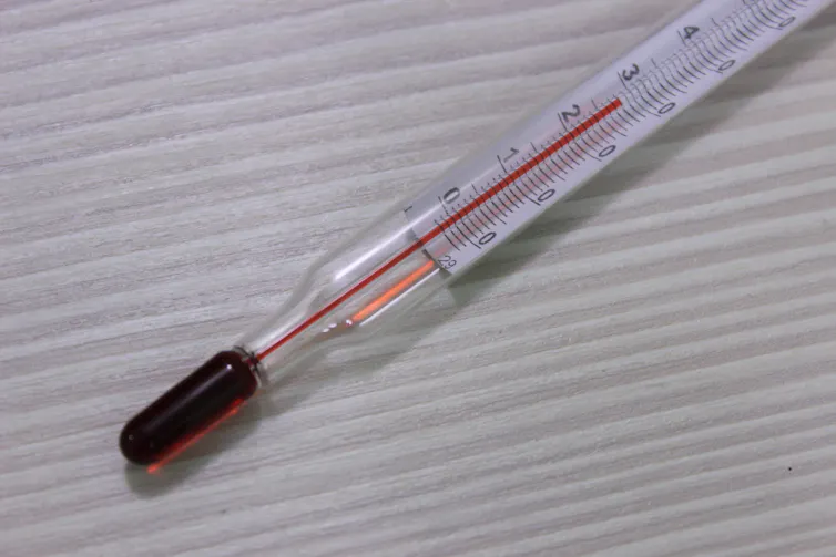 Thermometer with red liquid interior on a neutral background.
