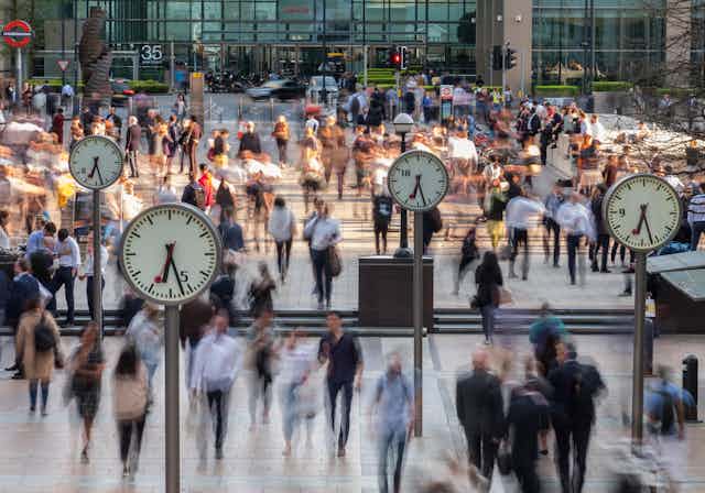 Blurred people walking through Canary Wharf with clocks in the foreground