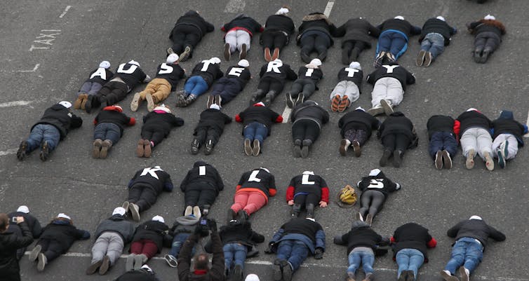 people lying down on concrete wearing letters that spell 'austerity kills'