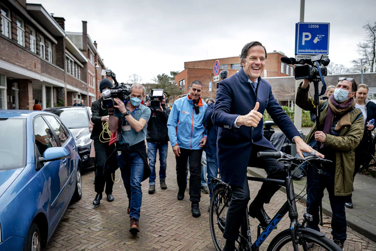 Dutch prime minister cycling down a street as press photographers follow him.