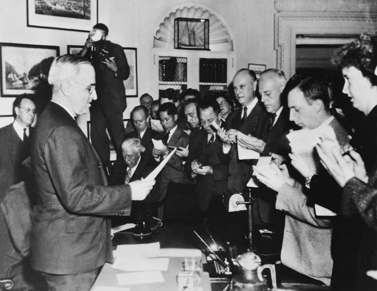 U.S. President Harry Truman at a desk in the White House, surrounded by reporters