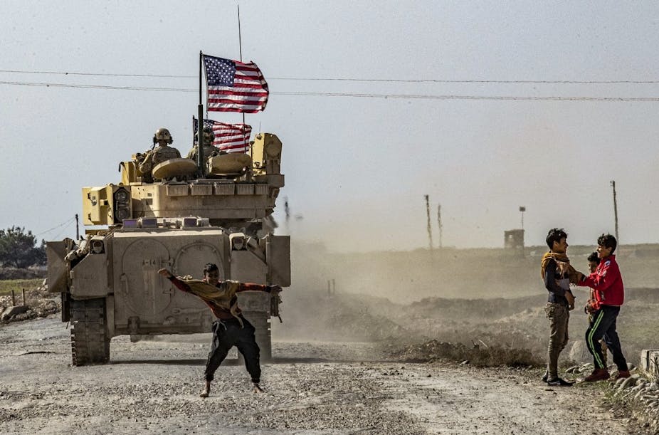 Des enfants jouent devant un véhicule de combat Bradley (BFV) américain en patrouille dans les champs pétrolifères de Suwaydiyah, dans la province de Hasakah (nord-est de la Syrie), le 13 février 2021.