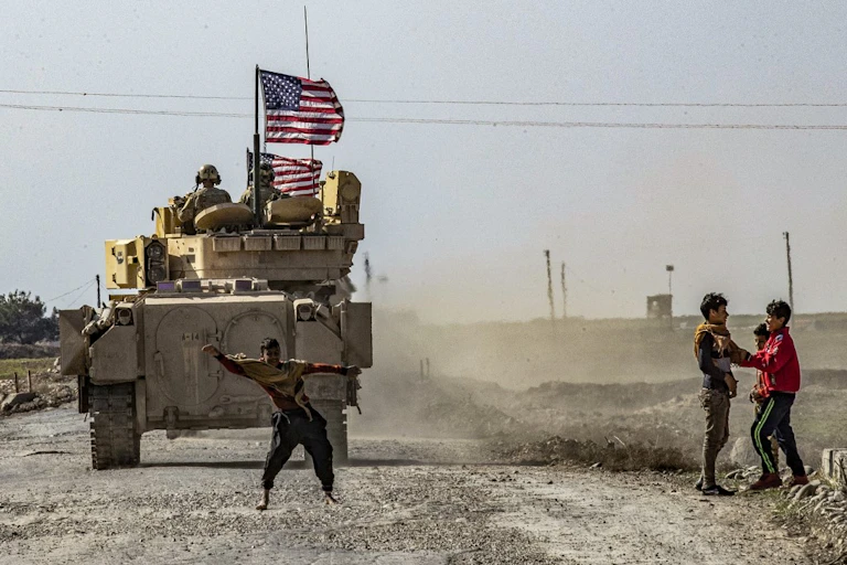 Des enfants jouent devant un véhicule de combat Bradley (BFV) américain en patrouille dans les champs pétrolifères de Suwaydiyah, dans la province de Hasakah (nord-est de la Syrie), le 13 février 2021.