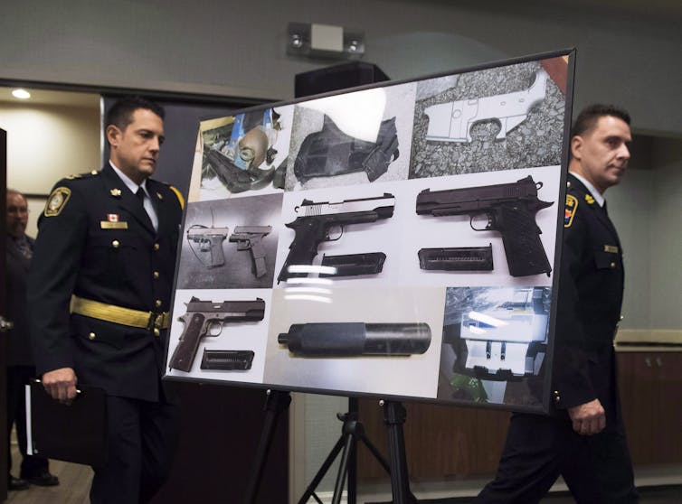 Police officers carry a billboard featuring photos of seized illegal firearms.