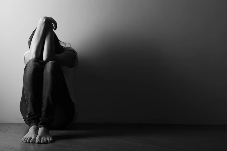 Woman sitting on ground with arms covering her face