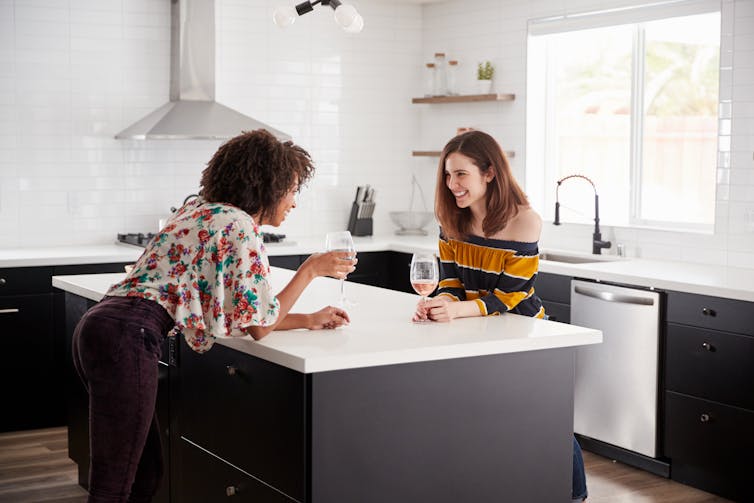 Two women drinking wine at a kitchen island bench.