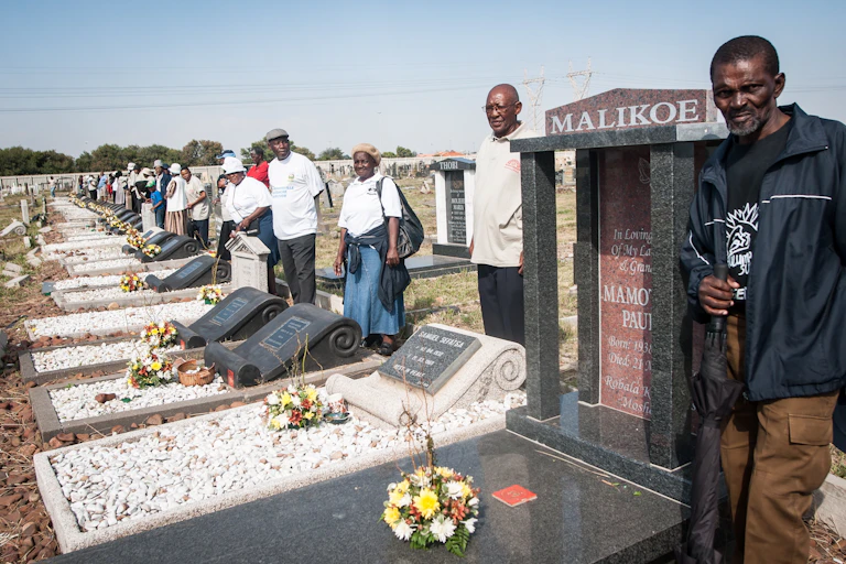 Men and women in a sombre mood stand behind a long line of graves.