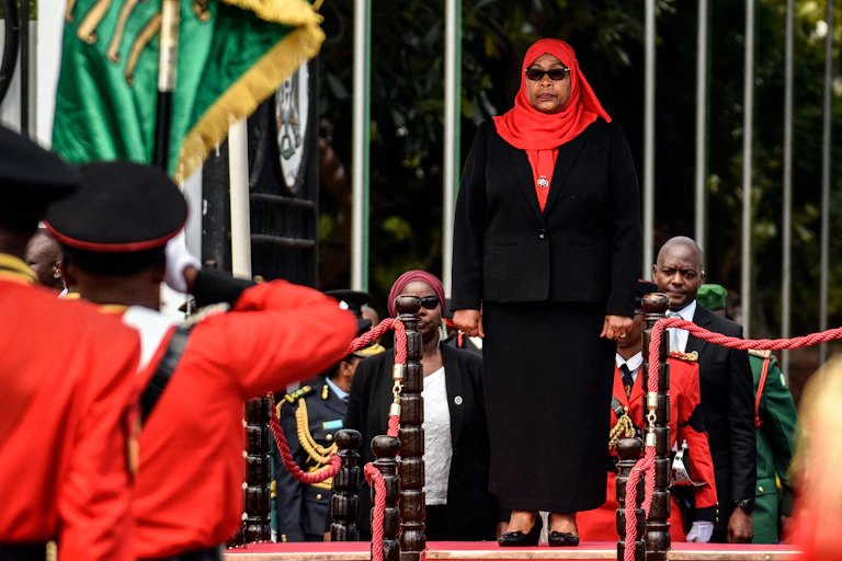 Black woman in a black skirt suit and a red head scarf stands on a podium