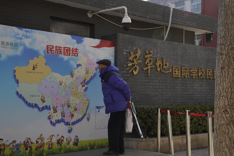 An elderly man looks at map of China showing different ethnic groups and the slogan 'Ethnic Unity.'
