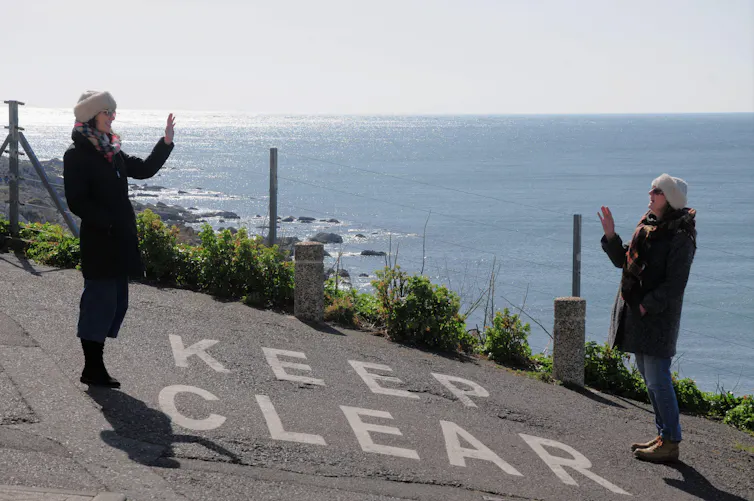 Two people wave to each other from a distance.