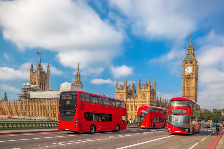Three red buses drive on Westminster Bridge in London.