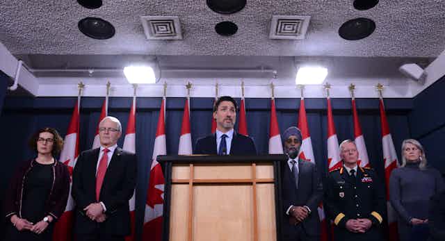 Justin Trudeau stands behind podium with ministers