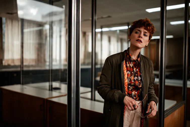 A woman in an office setting peers suspiciously into the distance.