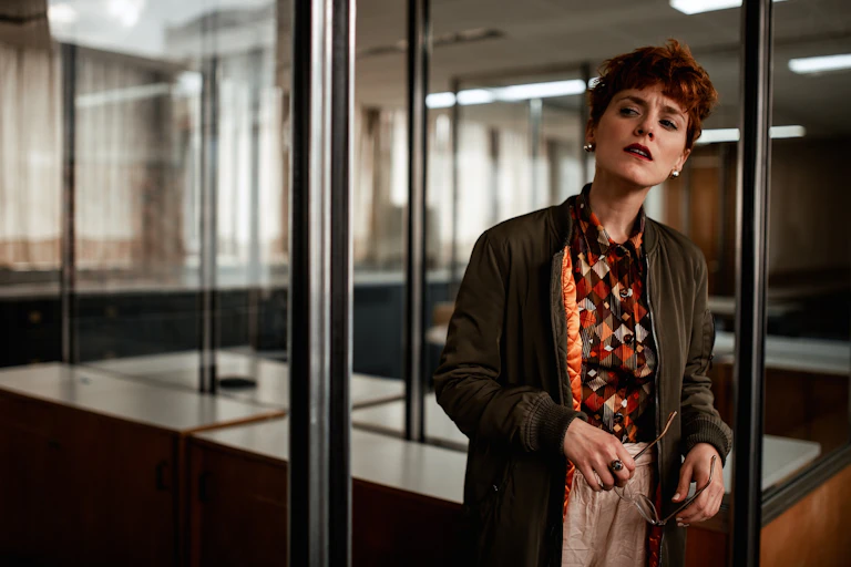 A woman in an office setting peers suspiciously into the distance.