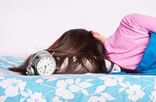 Person sleeping in bed with an alarm clock right next to their head