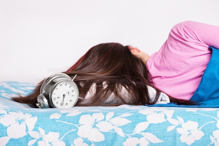 Person sleeping in bed with an alarm clock right next to their head