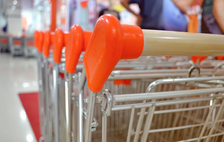 close up of shopping cart handles in foreground with grocery aisle out-of-focus in background