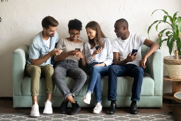 A group of four people sitting on a sofa looking at their phones.