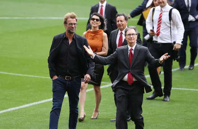 A group of men in suits and one woman walking across a football pitch.