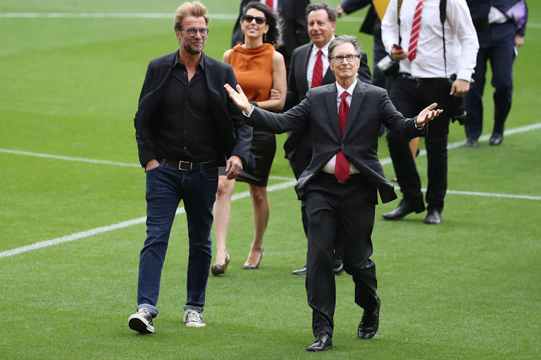 A group of men in suits and one woman walking across a football pitch.