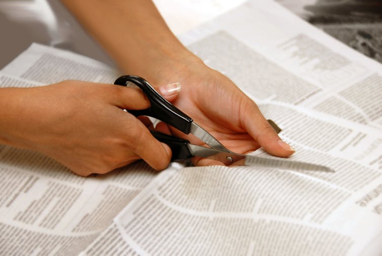 Hands cutting a newspaper.