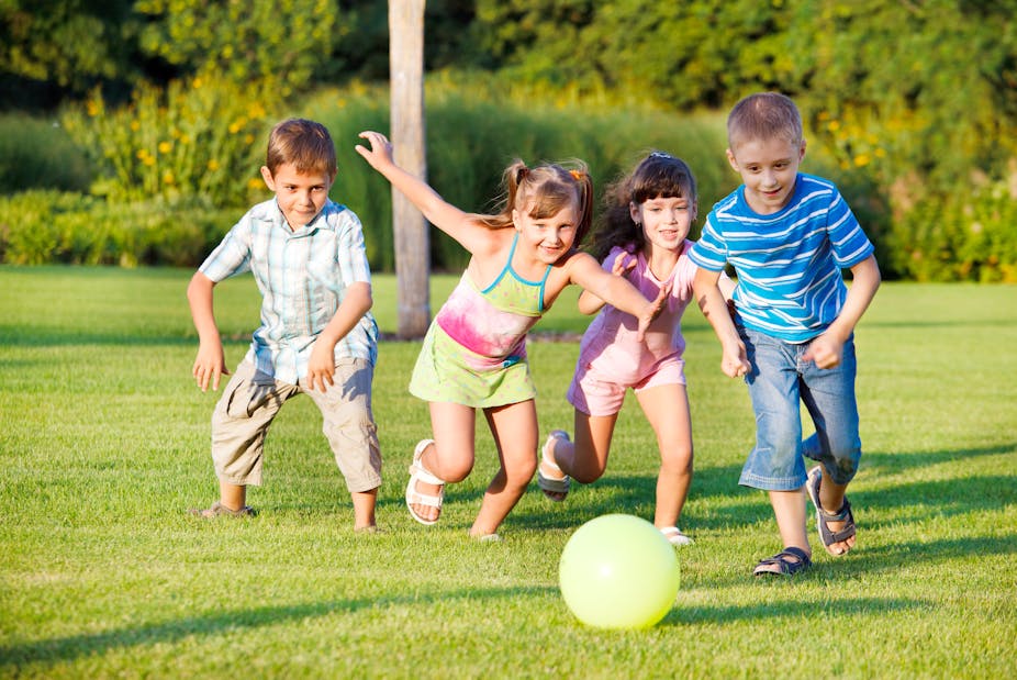 Four children chase after a ball in the park.