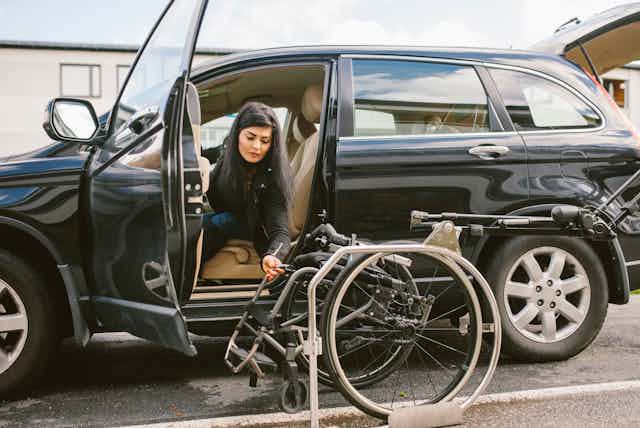 A woman holds a wheelchair next to a car