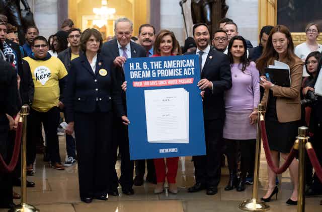 House Speaker Nancy Pelosi and Sen. Chuck Schumer, among others, smile while holding a poster celebrating the American Dream & Promise Act