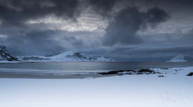Dark clouds form over a snowy landscape near the ocean