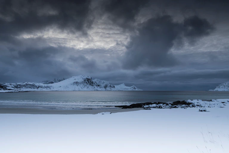 Dark clouds form over a snowy landscape near the ocean