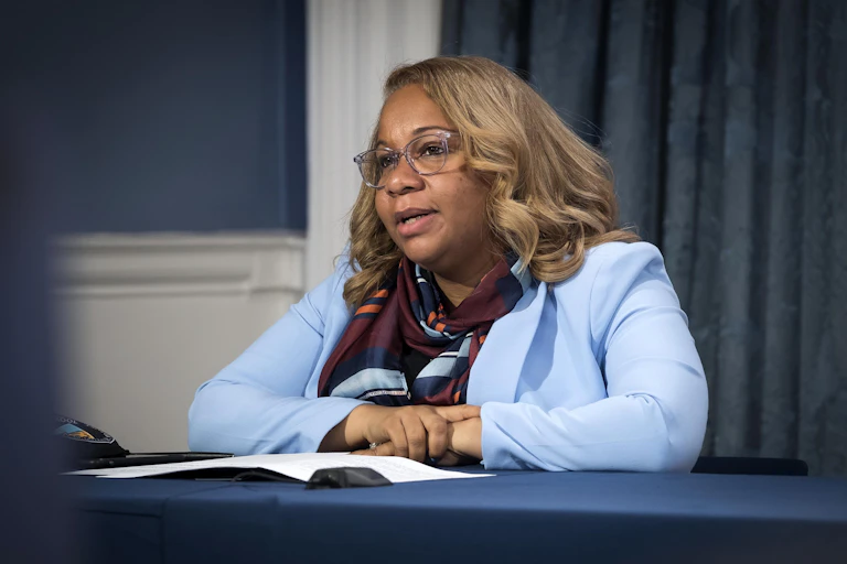 A woman speaks at a desk.