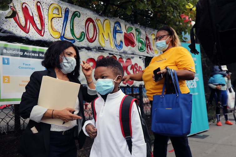 A group of school children and teachers wearing masks walk to school.