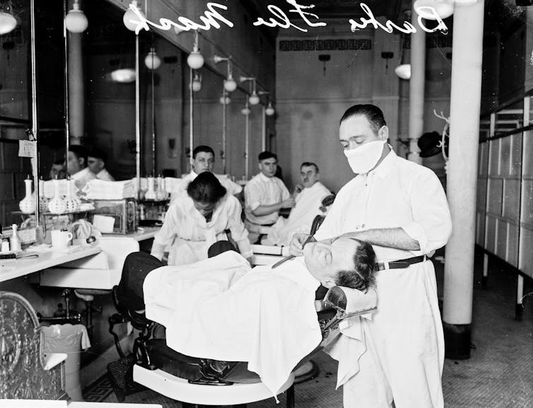 masked barber shaves a client