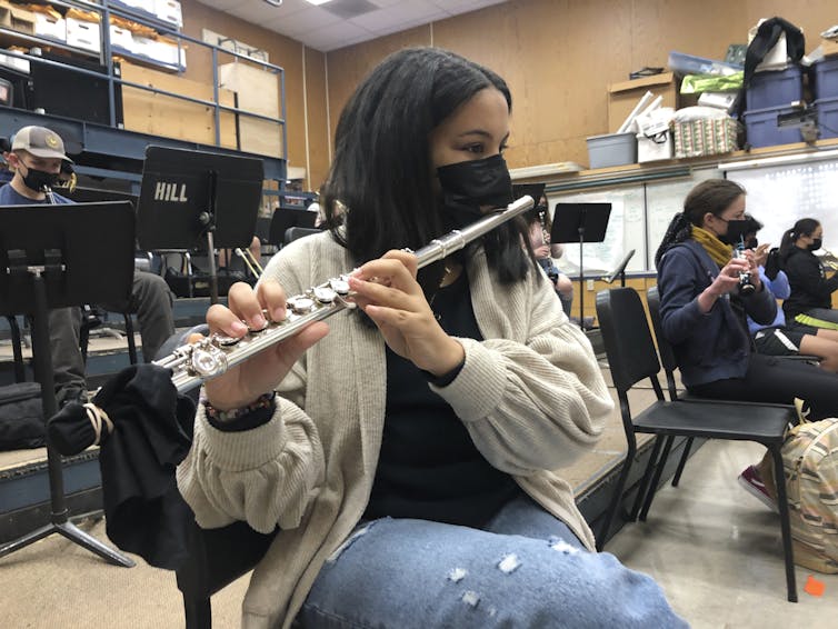 A student plays a flute through a mask during band practice.
