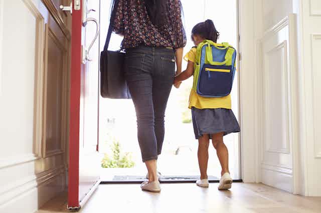 Mother and daughter with school bag on walking out the door.