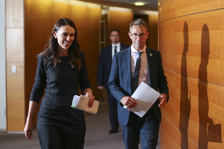 Jacinda Ardern and Ashley Bloomfield walking together in a parliamentary corridor