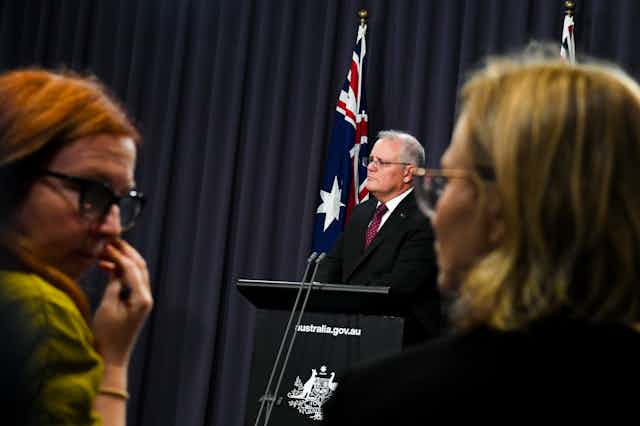 In the foreground, two female journalists, with Scott Morrison in the background