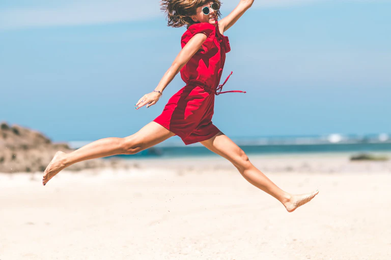 Woman in red jumpsuit jumping at the beach.
