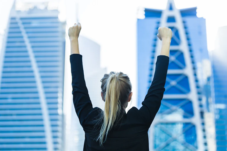 Young female executive with her hands in the air in front of some skyscrapers