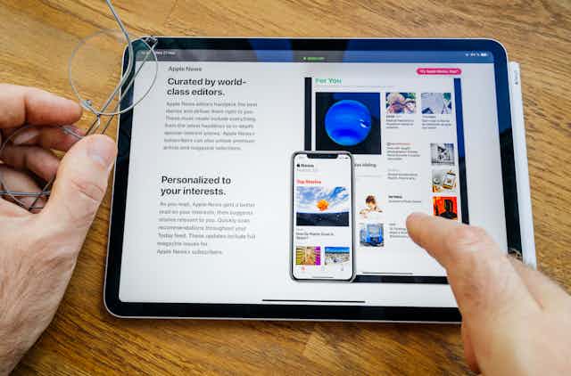 A tablet device showing Apple news and a user's fingers pointing to a news item. 