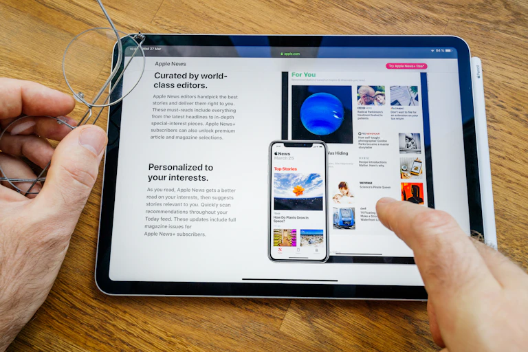 A tablet device showing Apple news and a user's fingers pointing to a news item.