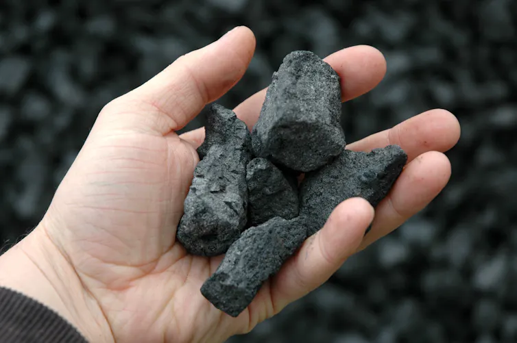 A hand holding clumps of black coke.