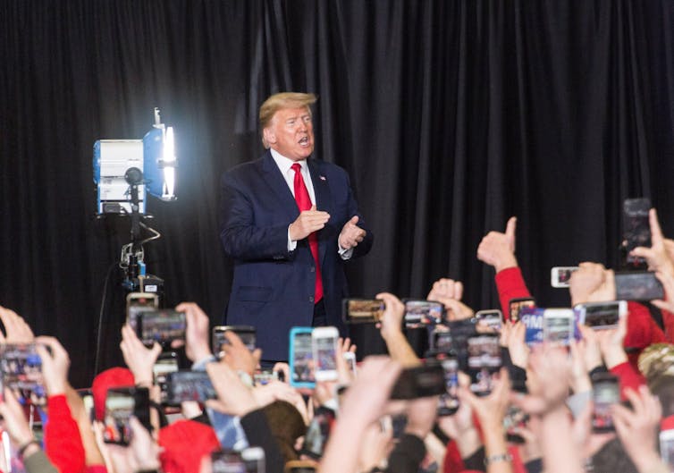 Donald Trump in front of a crowd holding up smartphones
