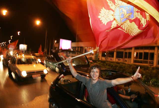 Young man waving a Montenegrin flag out the window of a car and smiling broadly