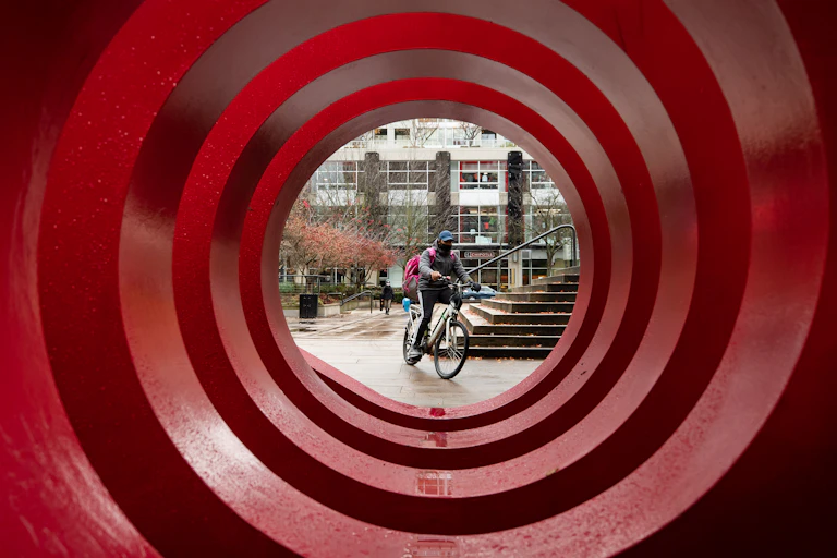 A food delivery worker wearing a face mask is framed by the red circles of a large public art installation.