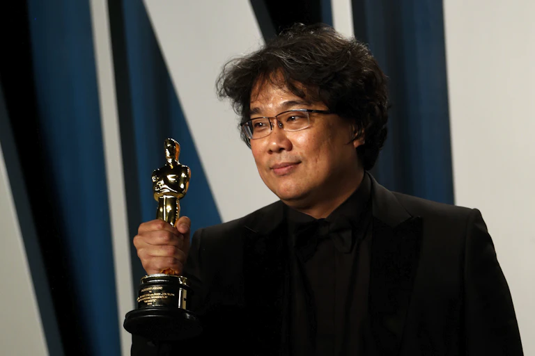 Korean man dressed in black holds Oscar trophy.