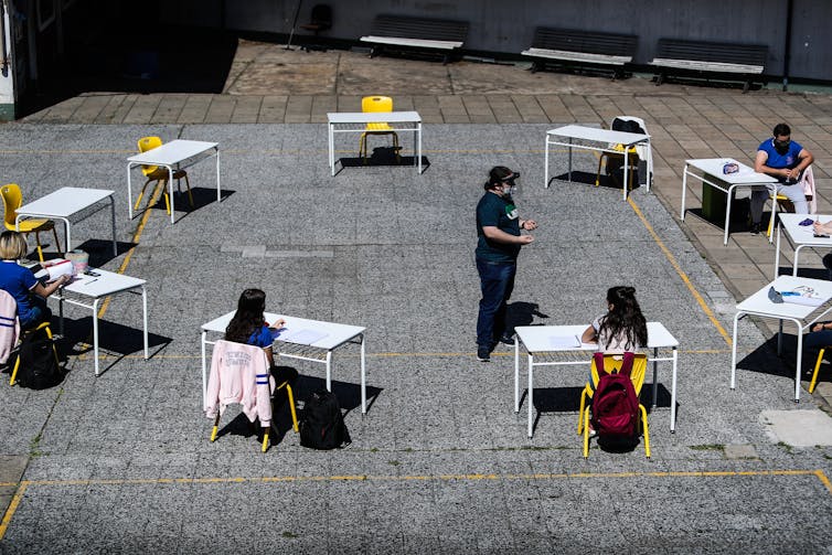 School children sit at desks arranged in a circle outdoors in Buenos Aires.