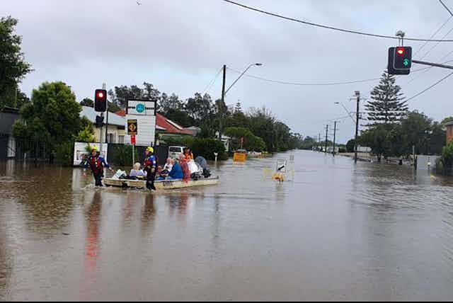 An emergency services rescue boat evacuates people along the flooded street of a town