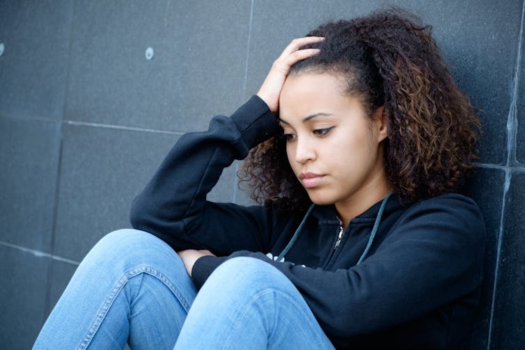 Young sad girl sitting against a wall.