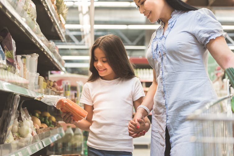 Mother and daughter looking at something in supermarket aisle.